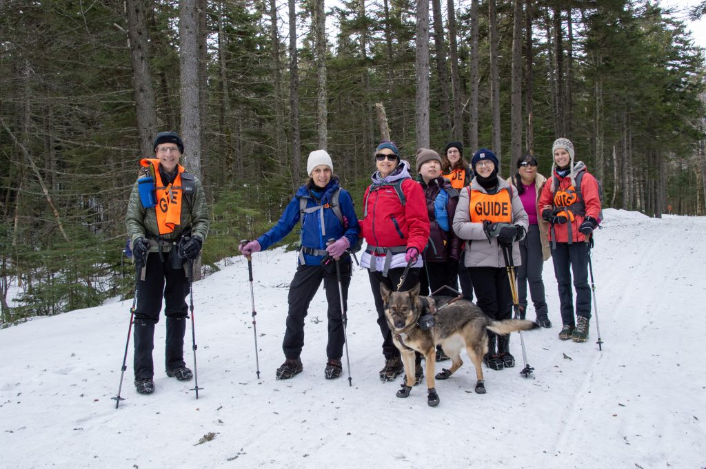 Group of skiiers wearing brightly colored jackets and smiling in the NH woods.